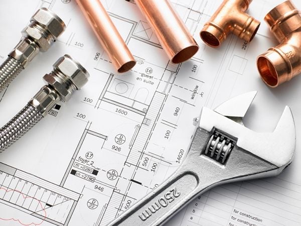 Plumbing tools and copper pipes arranged on architectural blueprints, including wrench and fittings